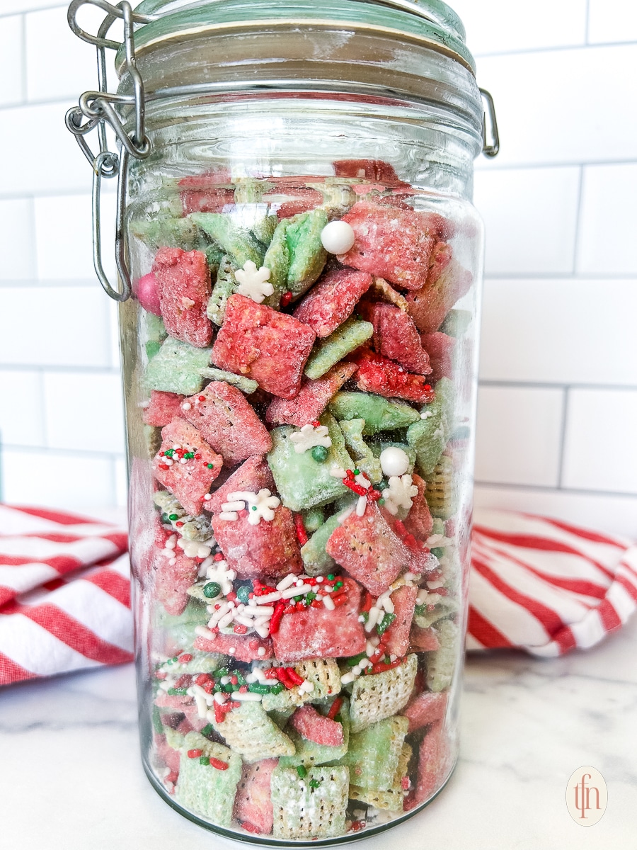 Christmas puppy chow in a tall glass canister on a marble countertop.