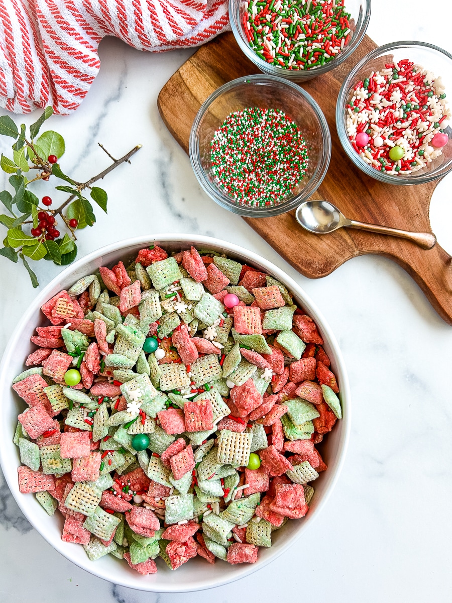 Large bowl of sweet and colorful cereal next to a smaller glass bowls of sprinkles on a white surface.