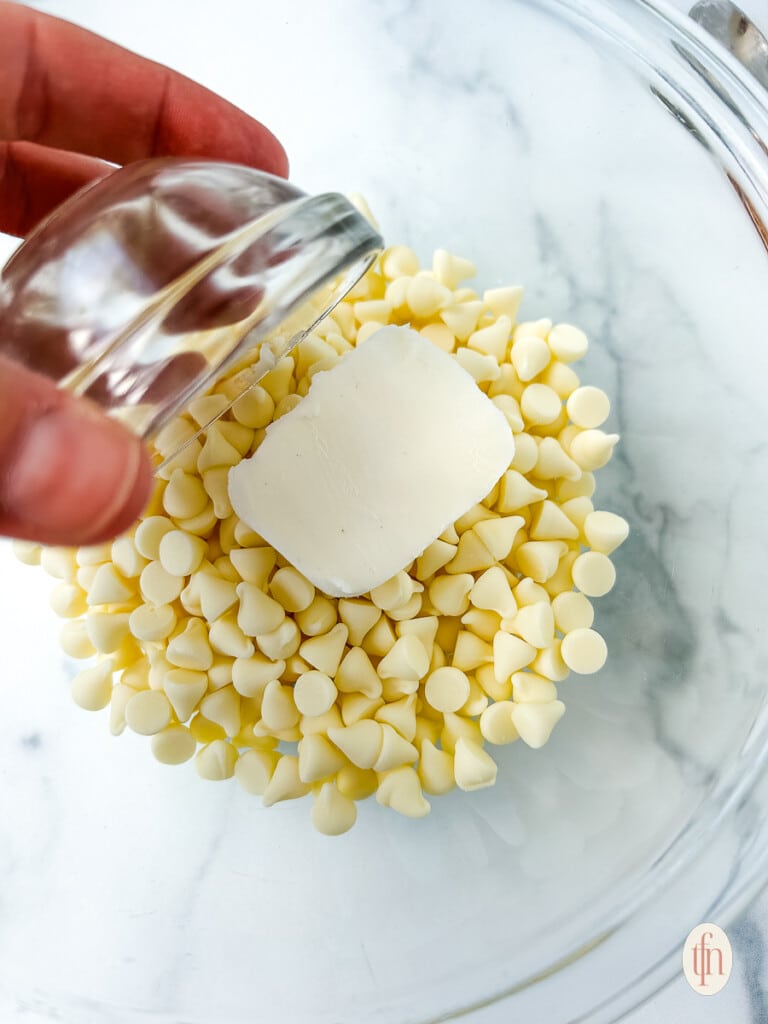 Adding Crisco shortening to white chocolate chips in a large glass bowl.