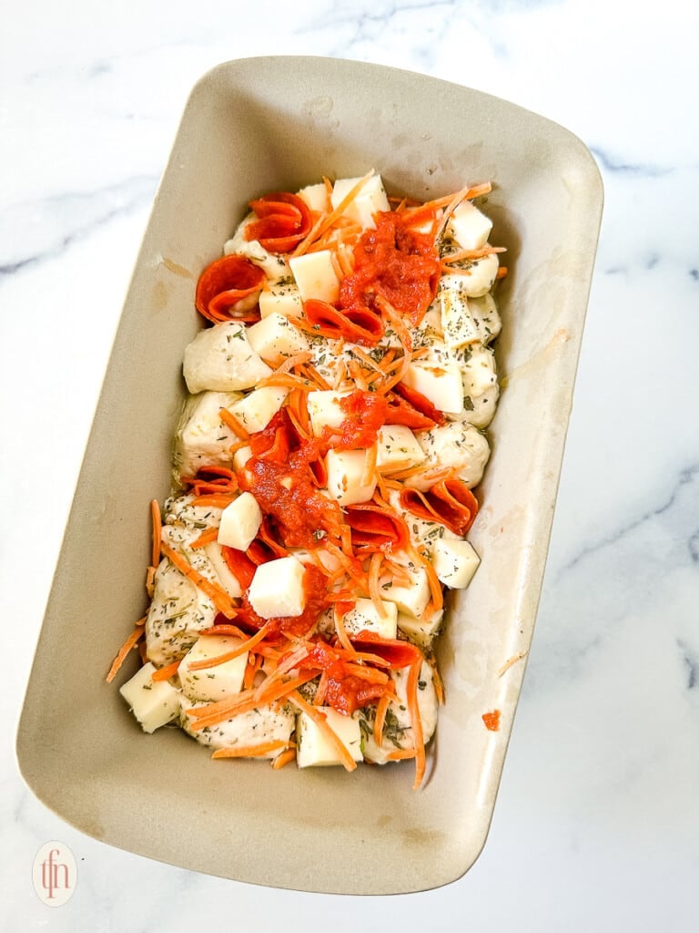 Assembling pull apart pizza bread in a baking pan.