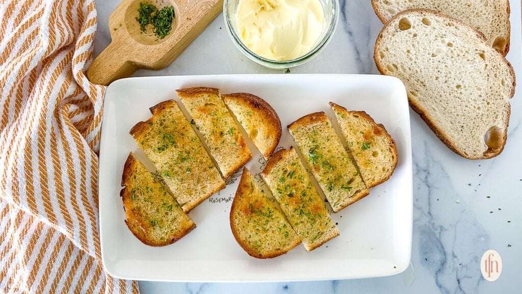 Two slices of garlic toast sliced on a white plate next to toppings. 