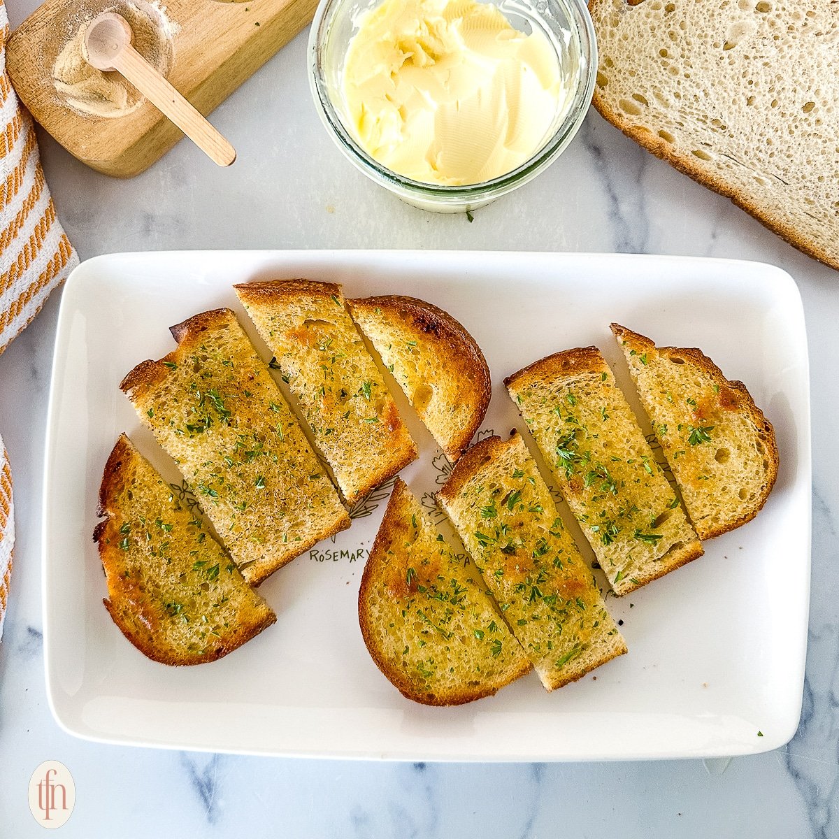 Two slices of garlic toast sliced on a white plate next to toppings.