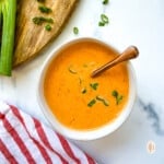 Copper spoon in a small dish of bang bang sauce with scallion garnish.