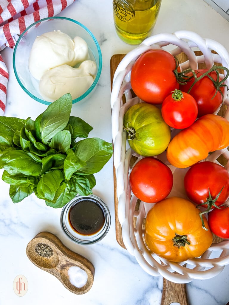 Basket full of garden tomatoes and fresh basil next to a bowl of burrata cheese for burrata caprese.