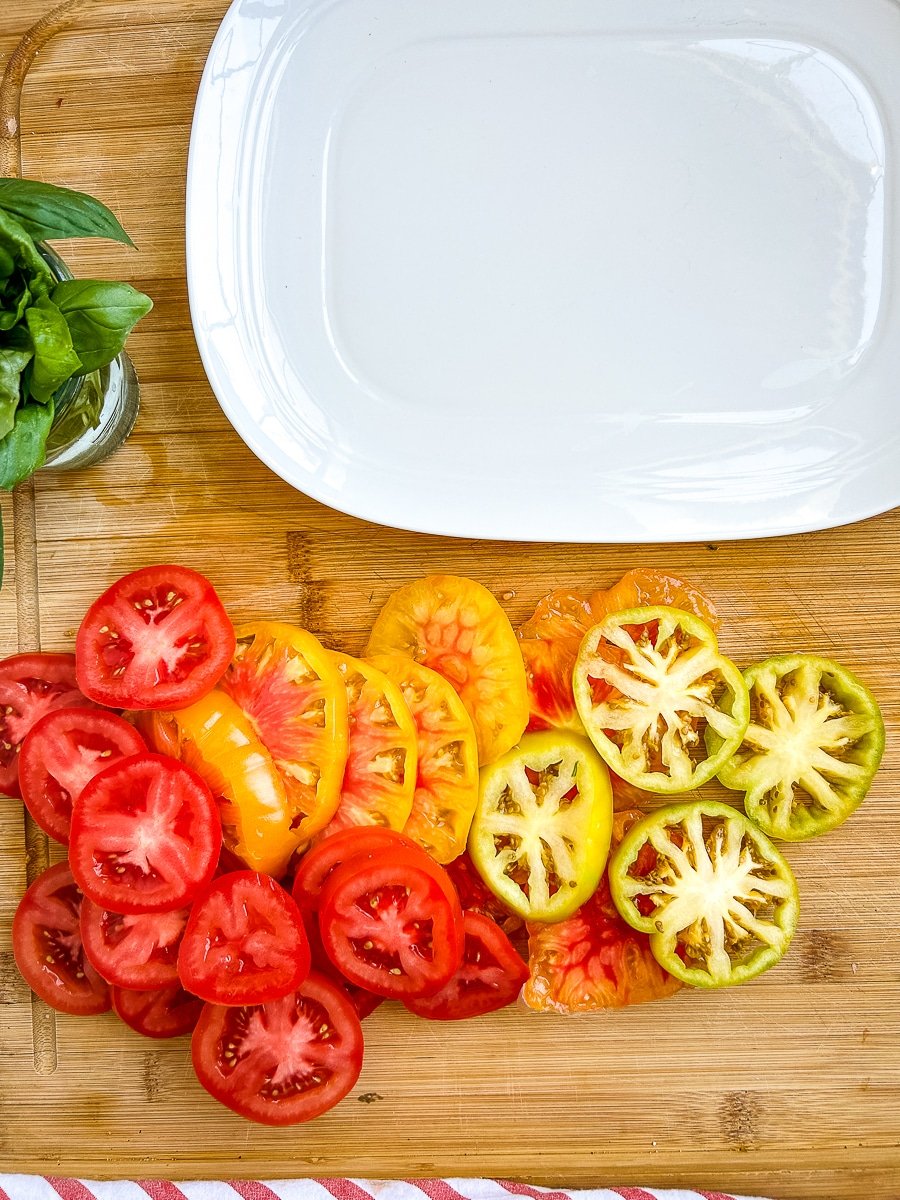 Empty white serving platter next to slices of heirloom tomatoes.
