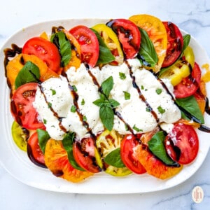 Platter of heirloom tomato salad with creamy white cheese and balsamic drizzle on top.