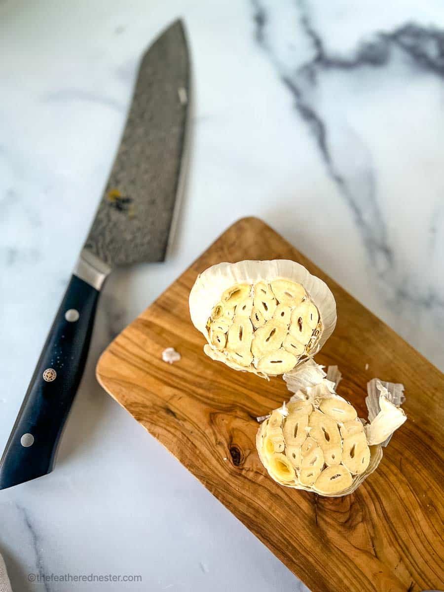 Head of garlic with the top cut off next to a knife on a white background.