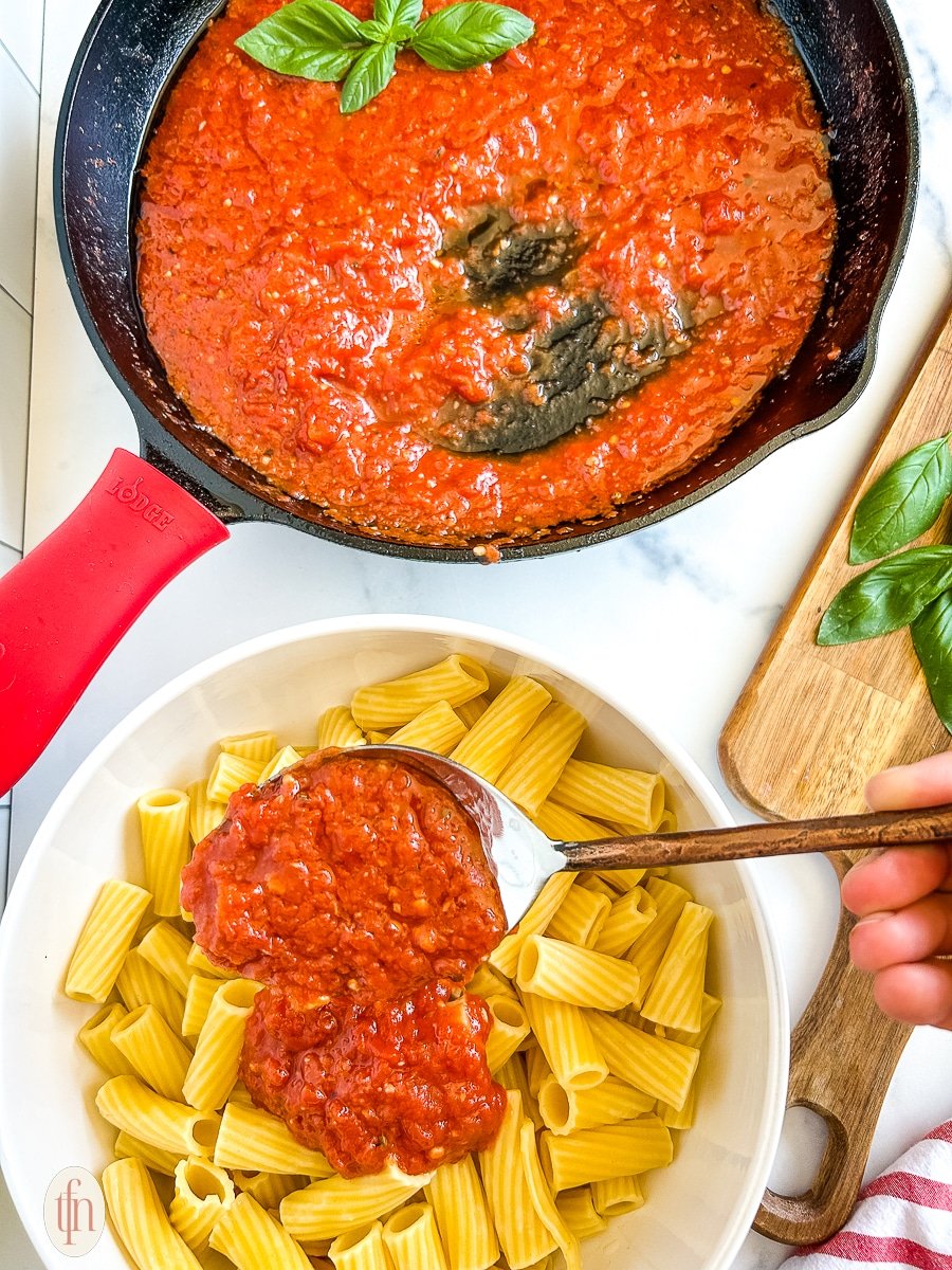 Spooning San Marzano tomato sauce over a bowl of ziti.