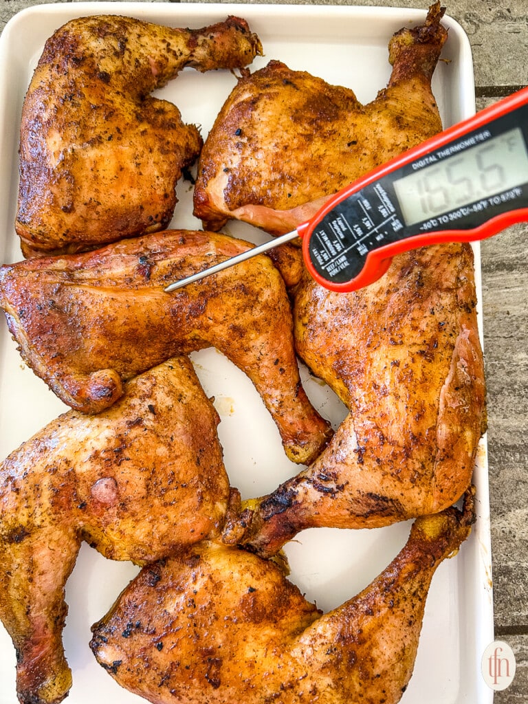 Chicken on a white platter being tested for temperature with an internal thermometer.