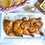 Platter of cooked chicken quarters on a white plate sprinkled with parsley flakes.
