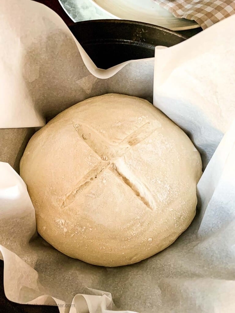 Risen dough with an 'x' on top in a parchment lined dutch oven.