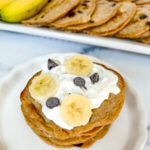 Banana chocolate chip pancakes with whipped topping and sliced bananas and chocolate chips on top.