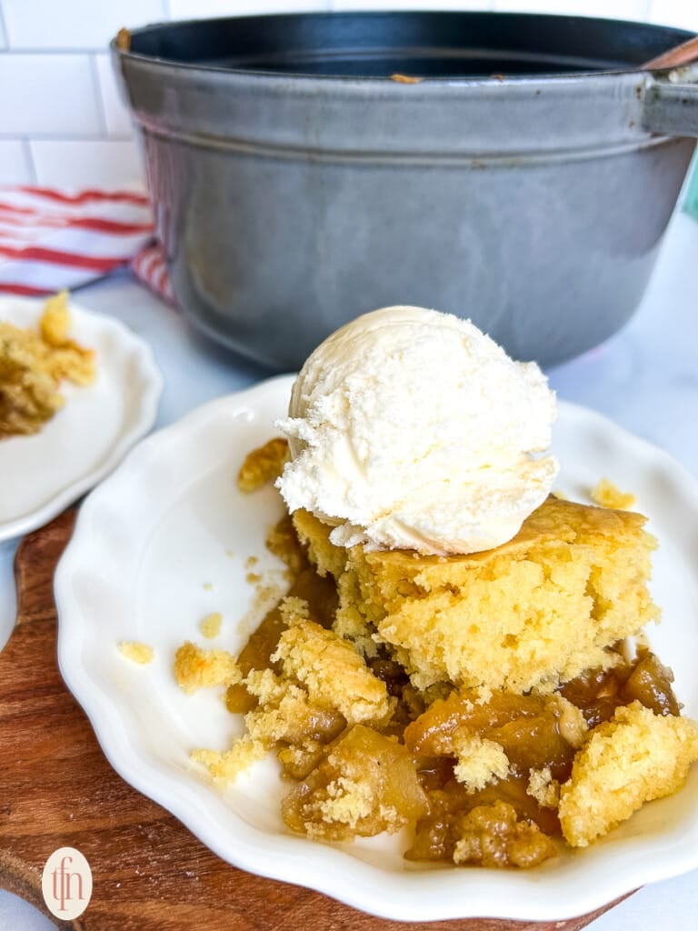 Apple cobbler with ice cream on top on a white plate.