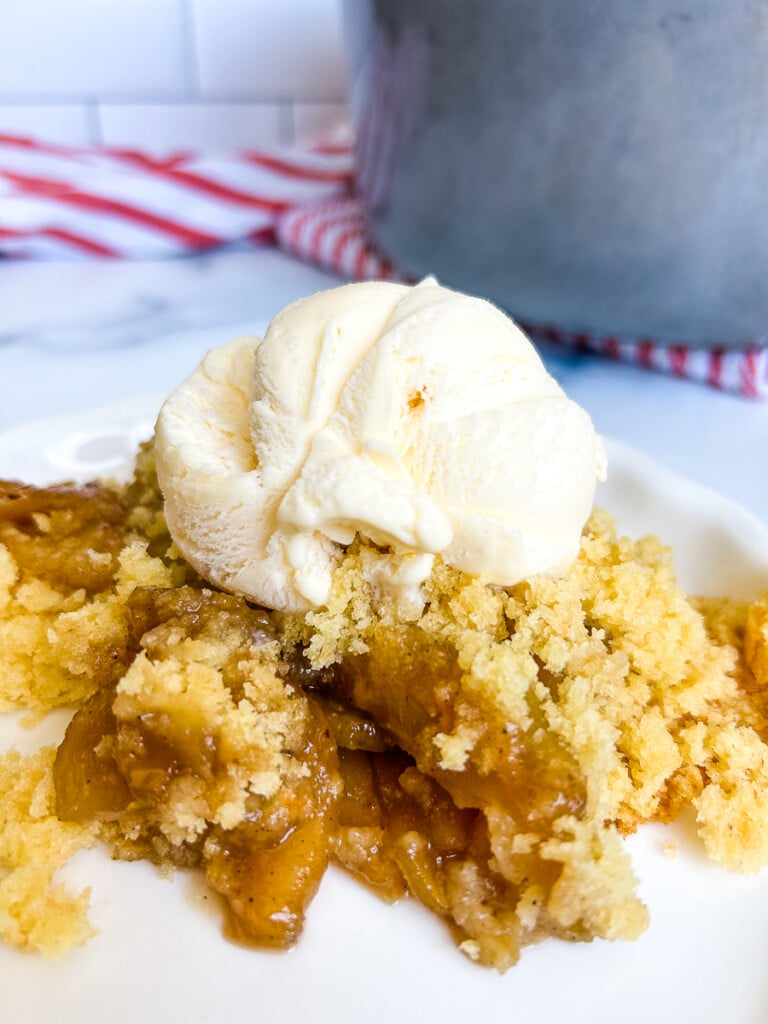 Apple cobbler with ice cream on top on a white plate.