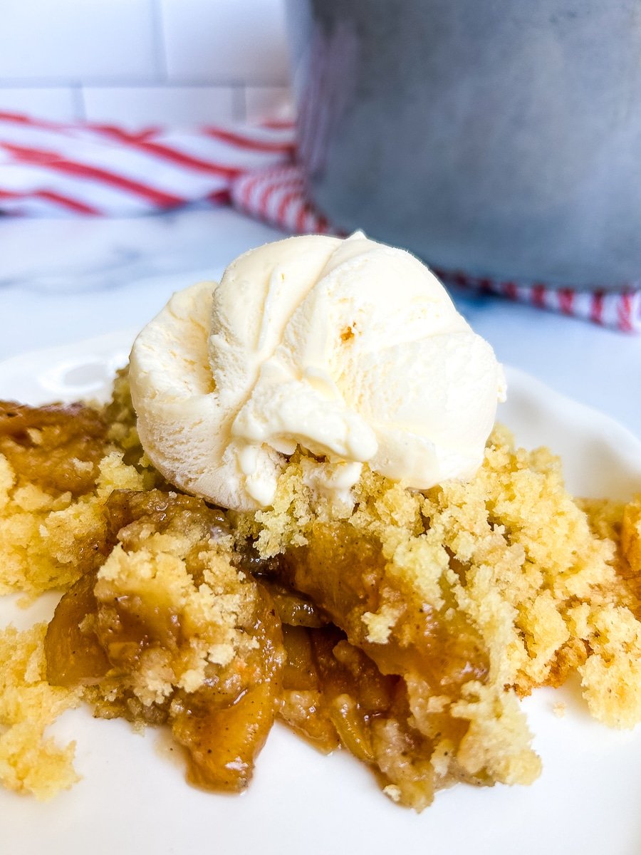 Apple cobbler with ice cream on top on a white plate.