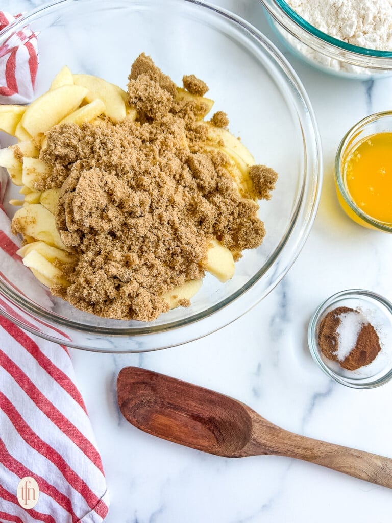 Sliced apples in a glass bowl with brown sugar on top.