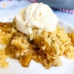 Apple cobbler with ice cream on top on a white plate.