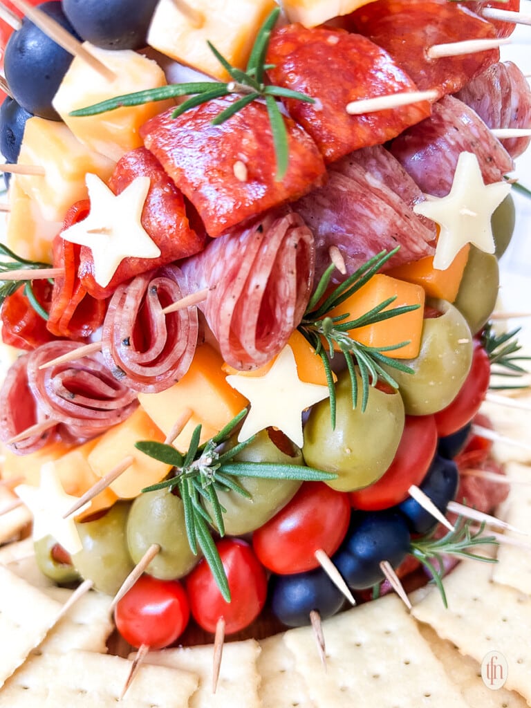Close up of a charcuterie tree with meats, cheeses, olives, and stars stuck into a styrofoam cone with toothpicks.