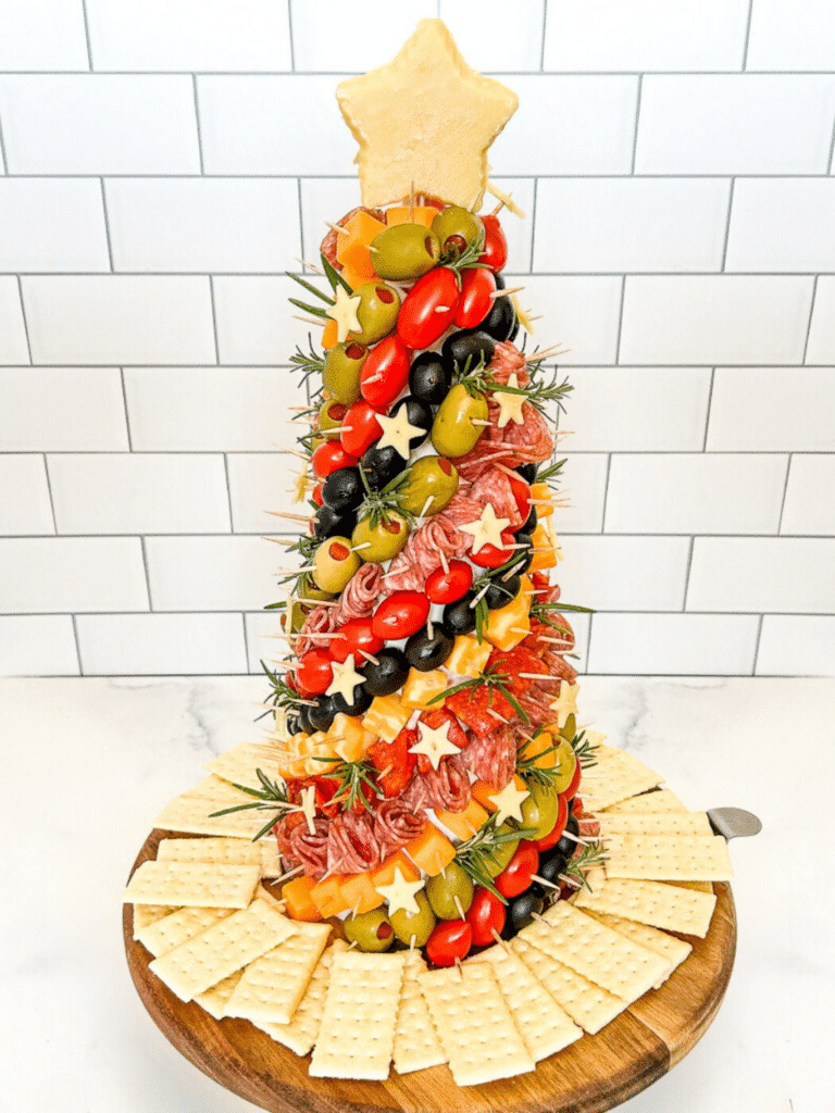 Decorated charcuterie tree standing vertically on a platter with a white background.