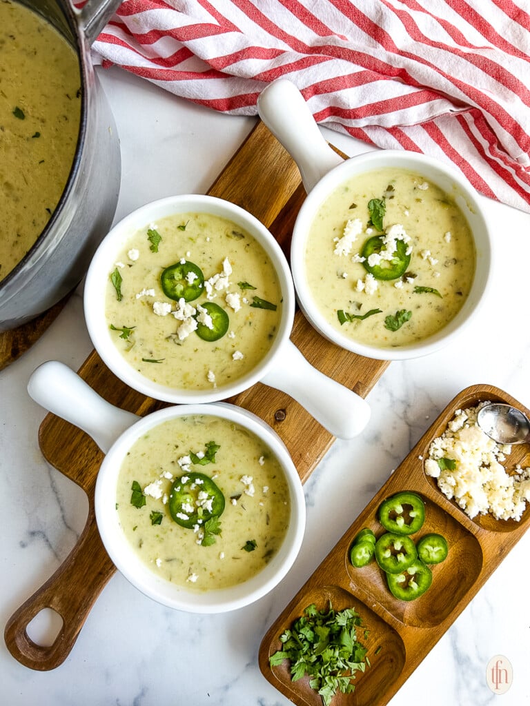 Three bowls of cream of jalapeno soup on a cutting board on a white background.