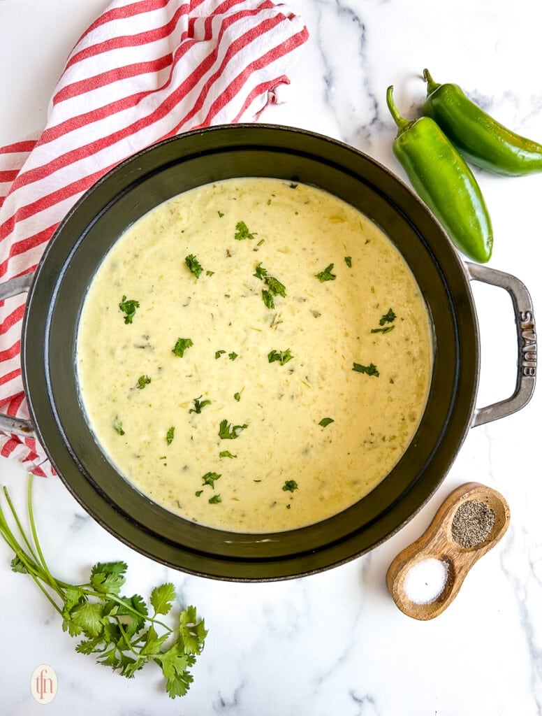 Overhead image of cream of jalapeno soup in a pot on a white surface.