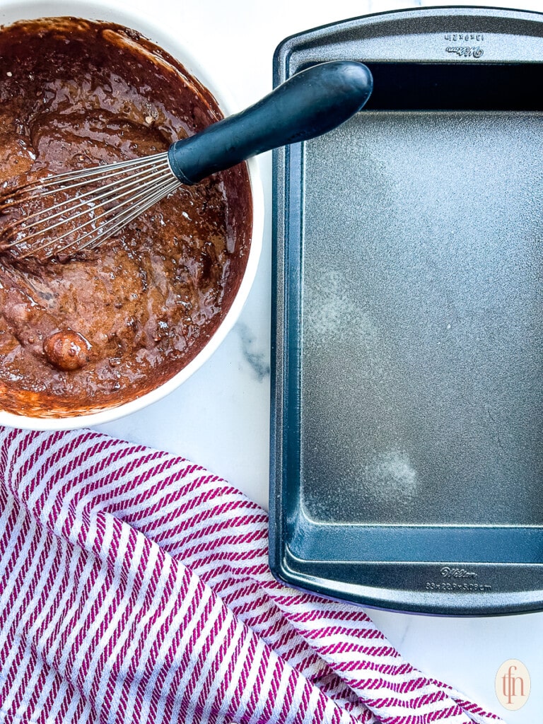 Chocolate cake batter sitting next to an empty baking tray.