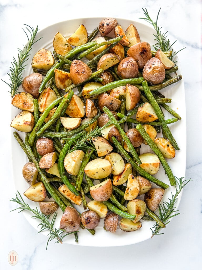 Platter of roasted green beans and potatoes on a white background.