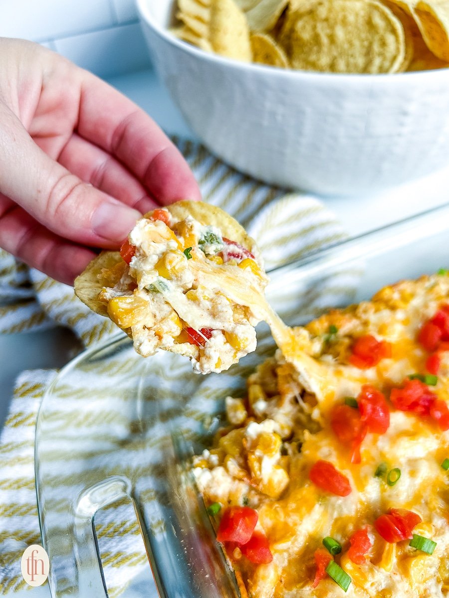 Chip with dip held above the plate of casserole.