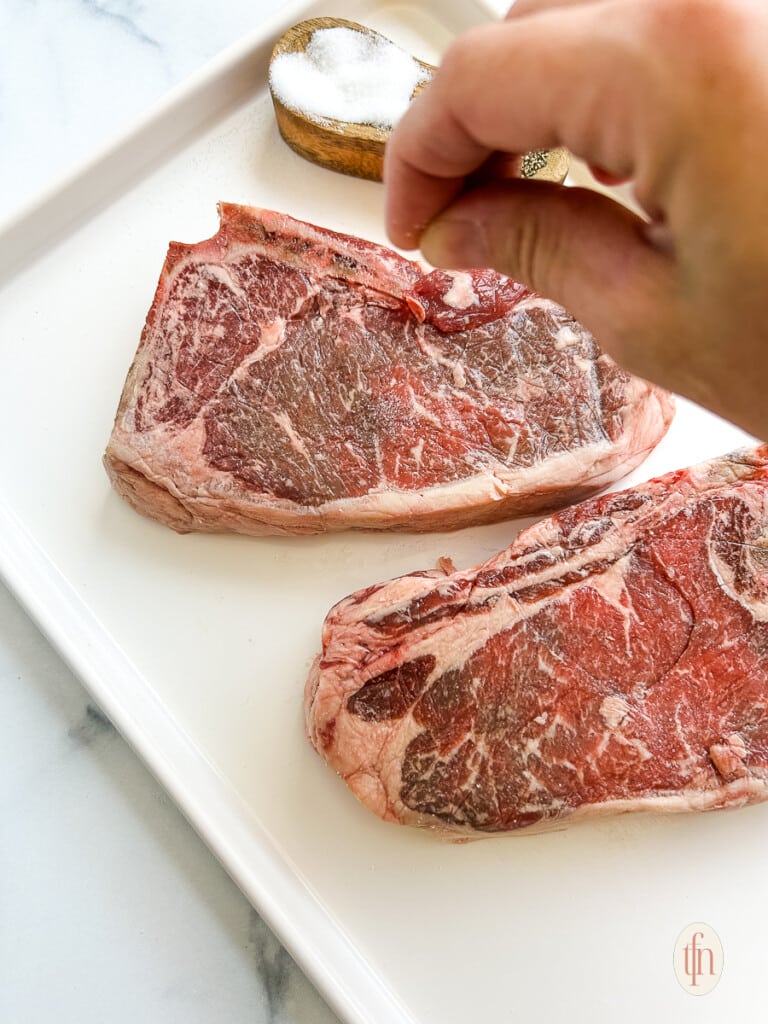 Seasoning strip steaks with salt.