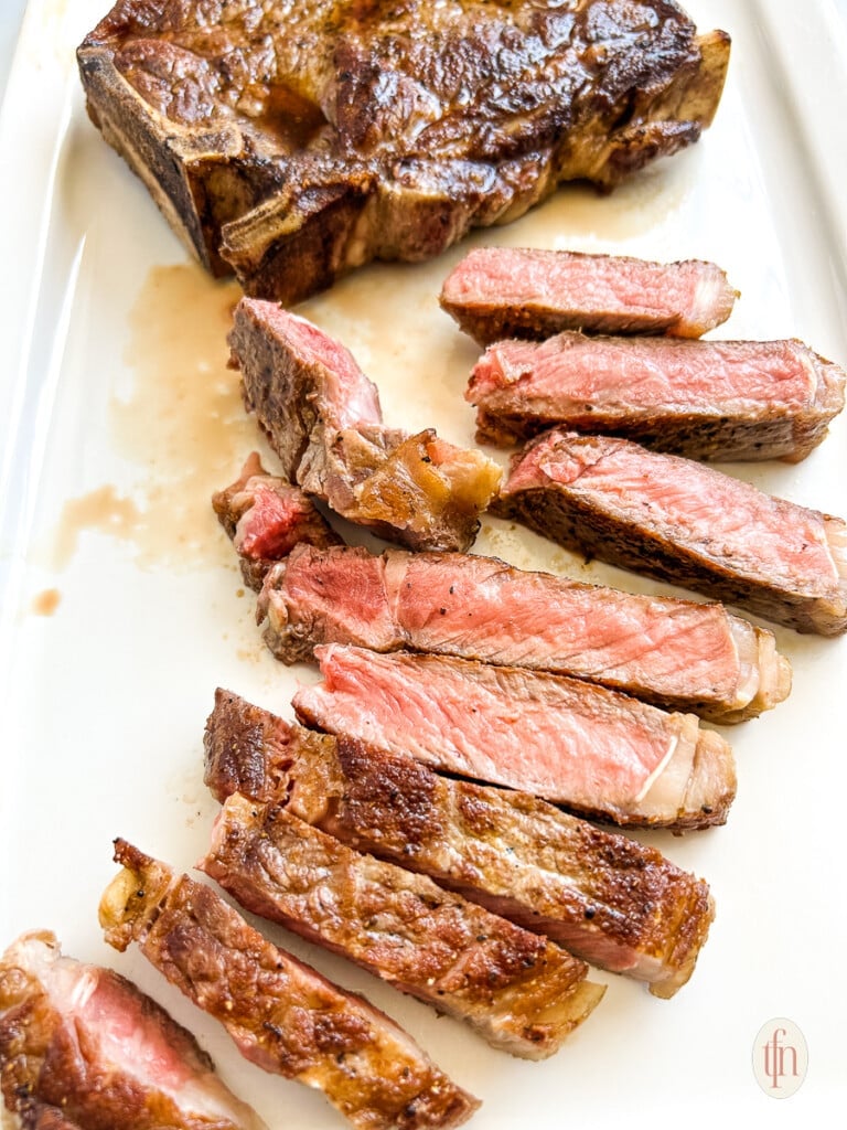 Slices of grilled strip steak on a white platter.
