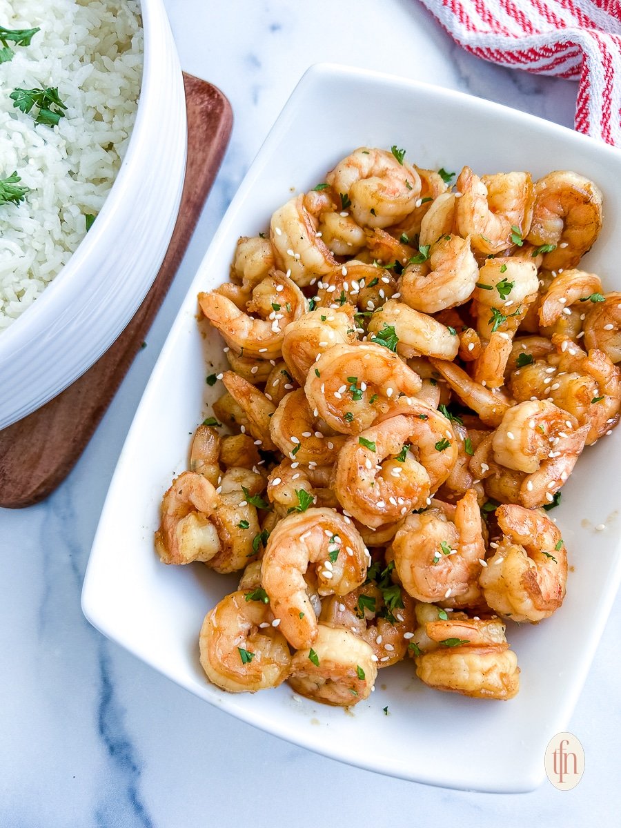 Blackstone hibachi shrimp on a white platter next to a bowl of white rice.