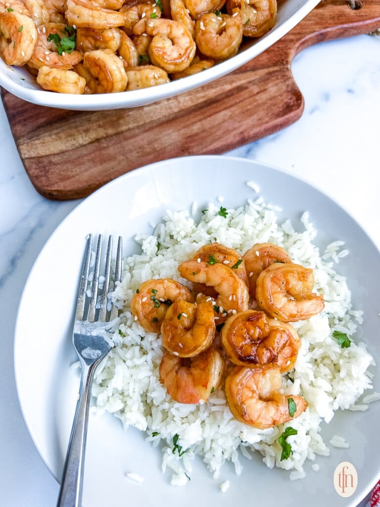 A bowl of shrimp on top of white rice with a fork next to it.
