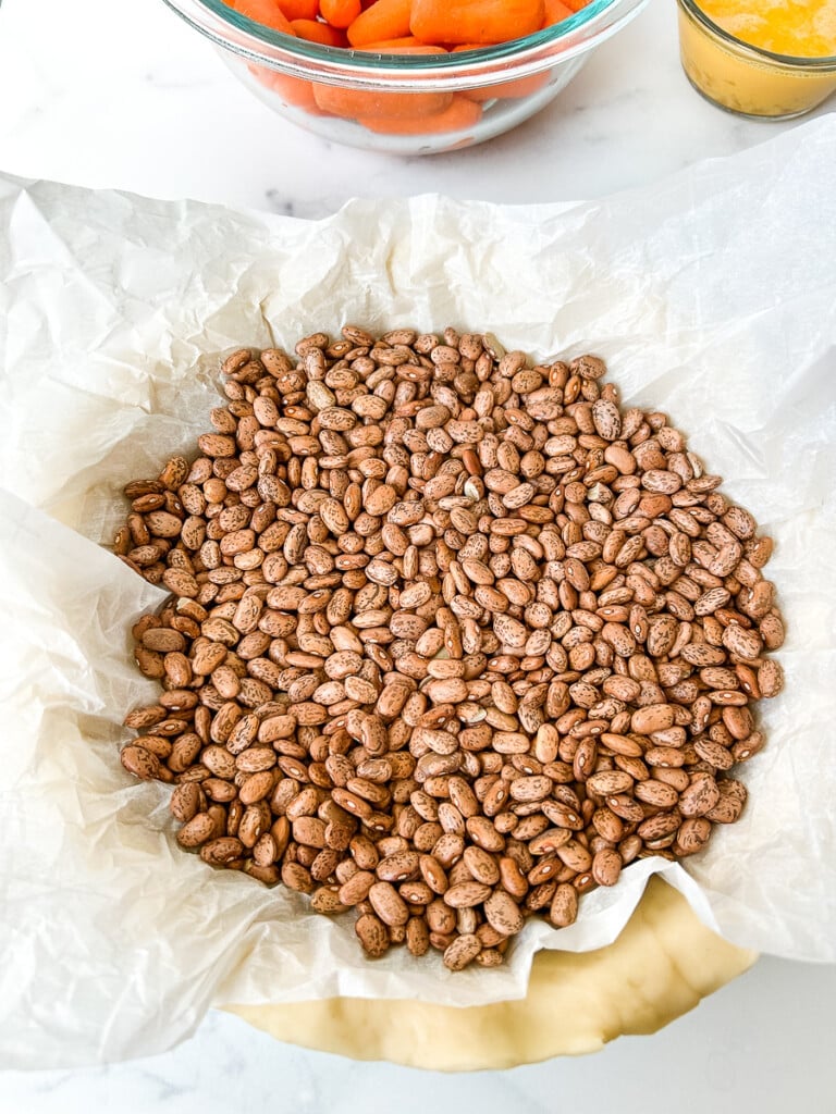 An unbaked pie crust topped with parchment paper and dried beans.