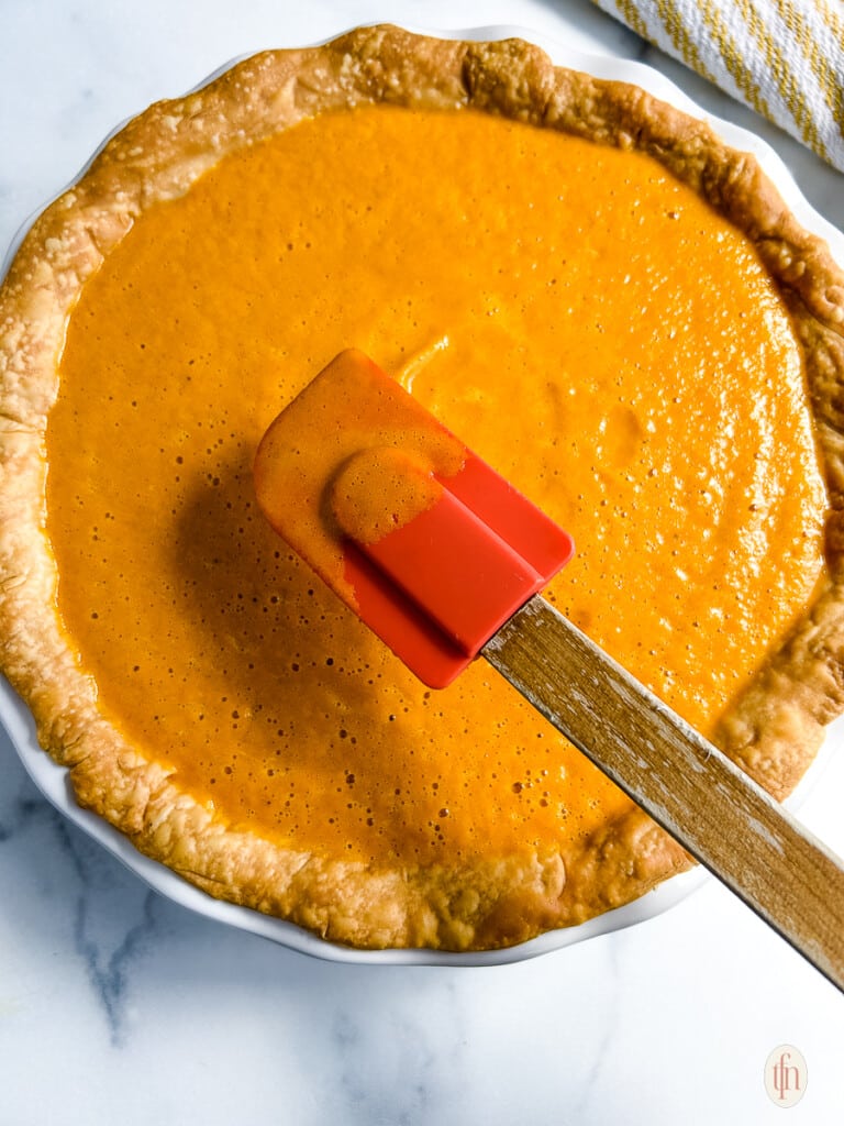 Spatula smoothing top of carrot pie.