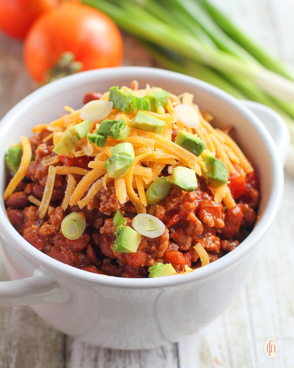 Chili in a white bowl with tomatoes and green onions.