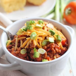 Soup bowl filled with homemade stovetop chili, garnished with shredded cheddar cheese and chopped scallions.