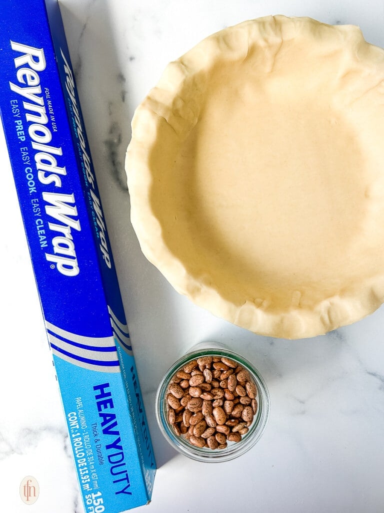 Reynolds wrap next to unbaked pie crust and a jar of dried beans.