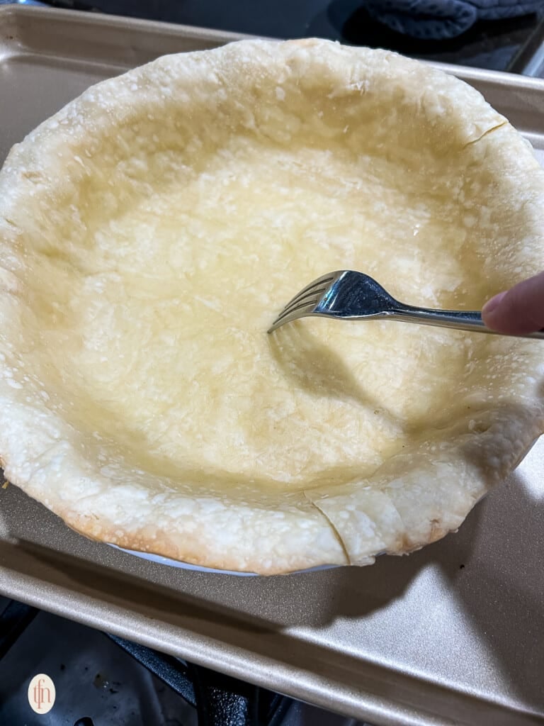 Fork poking holes in a partially baked pie crust.