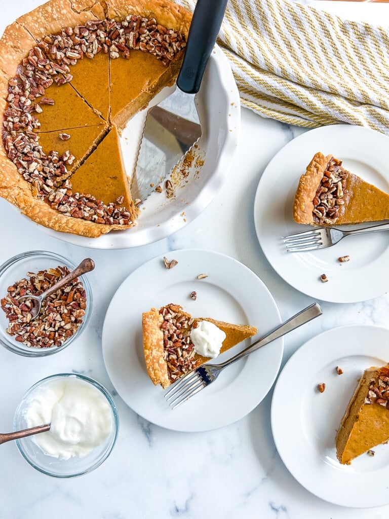 Slices of pumpkin pie on plates next to a whole pie with slices cut out.