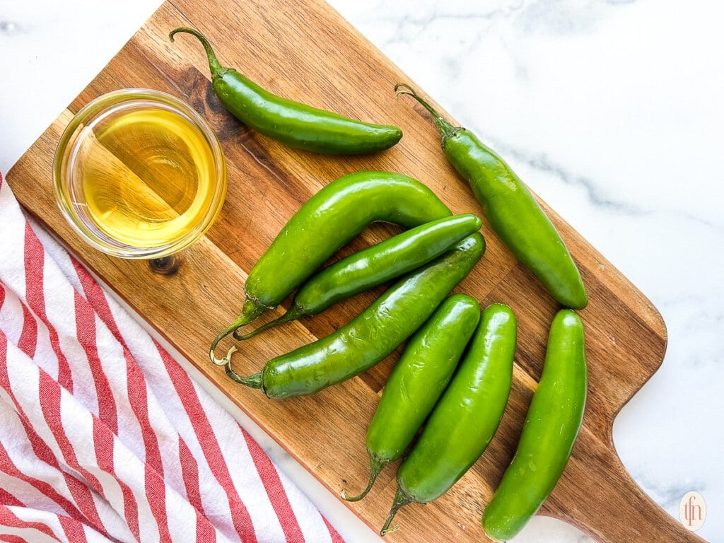 Whole green jalapenos next to a dish of olive oil for roasting in oven.