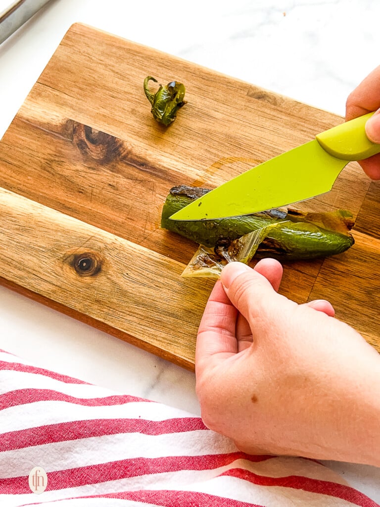 Woman using a knife to remove blistered skin from an oven roasted green pepper.