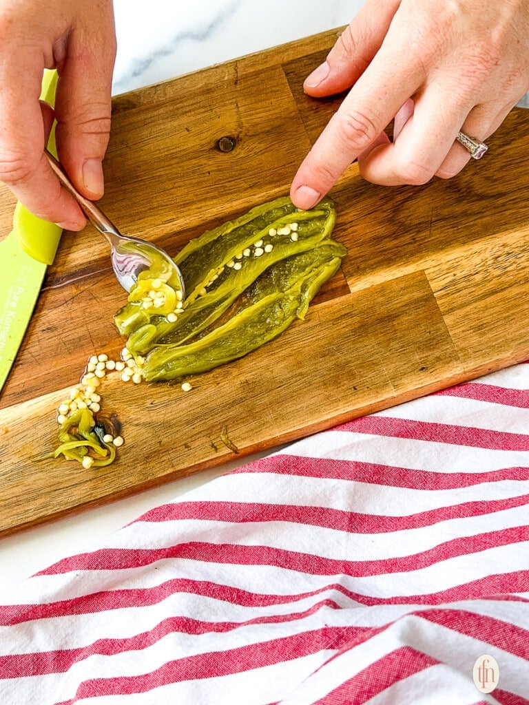 Using a spoon to remove seeds from a roasted jalapeno.