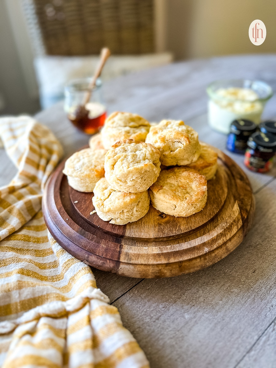 Biscuits piled on a wooden serving platter on a table.