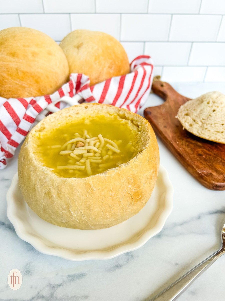 Sourdough bread bowl filled with soup on a white plate on a white background.