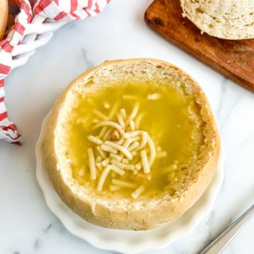 Sourdough bread bowl filled with soup on a white plate on a white background.