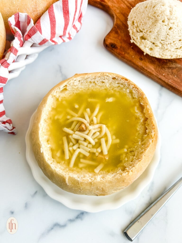 Sourdough bread bowl filled with soup on a white plate on a white background.