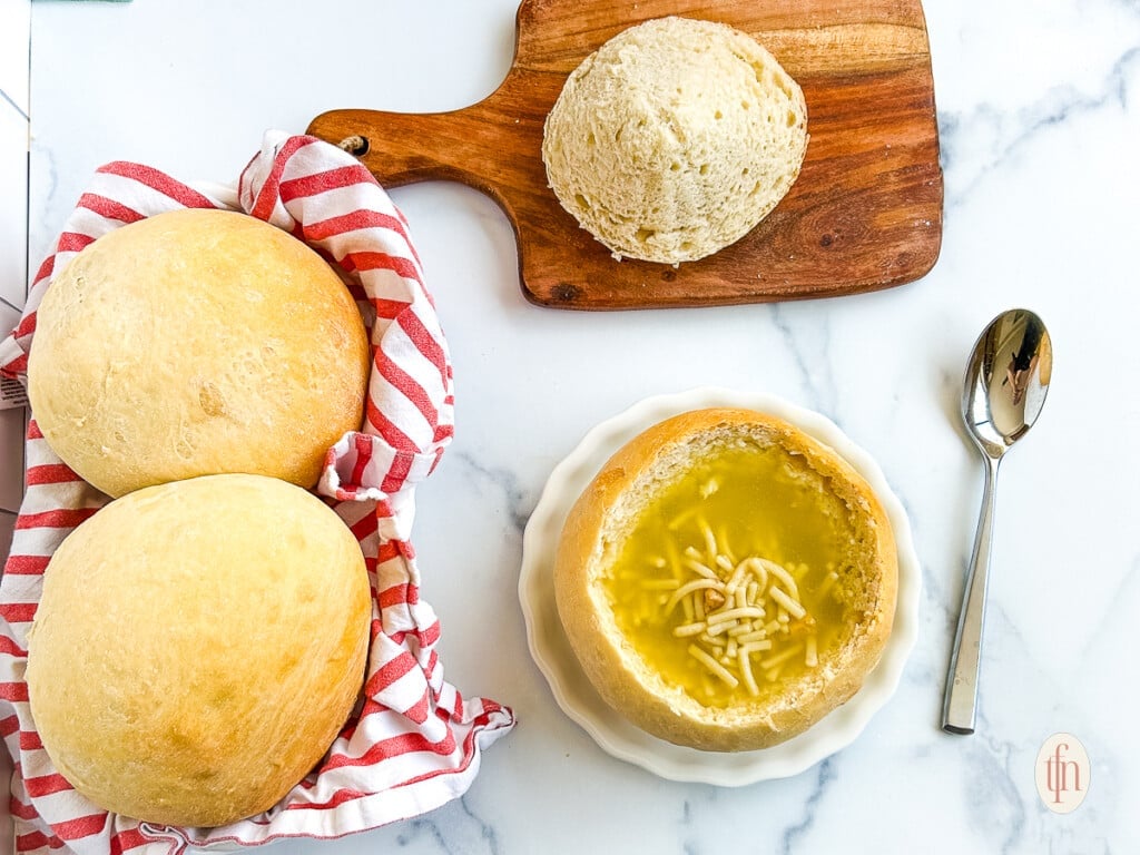 Sourdough bread bowl filled with soup on a white plate on a white background.