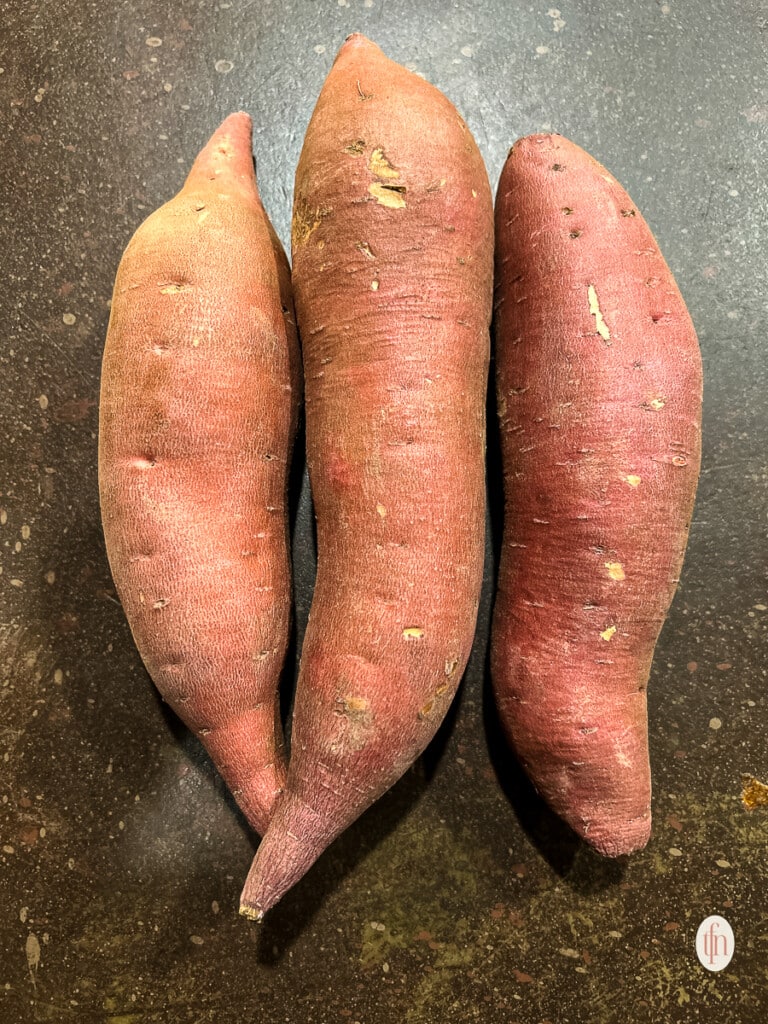 Three large sweet potatoes on a counter.