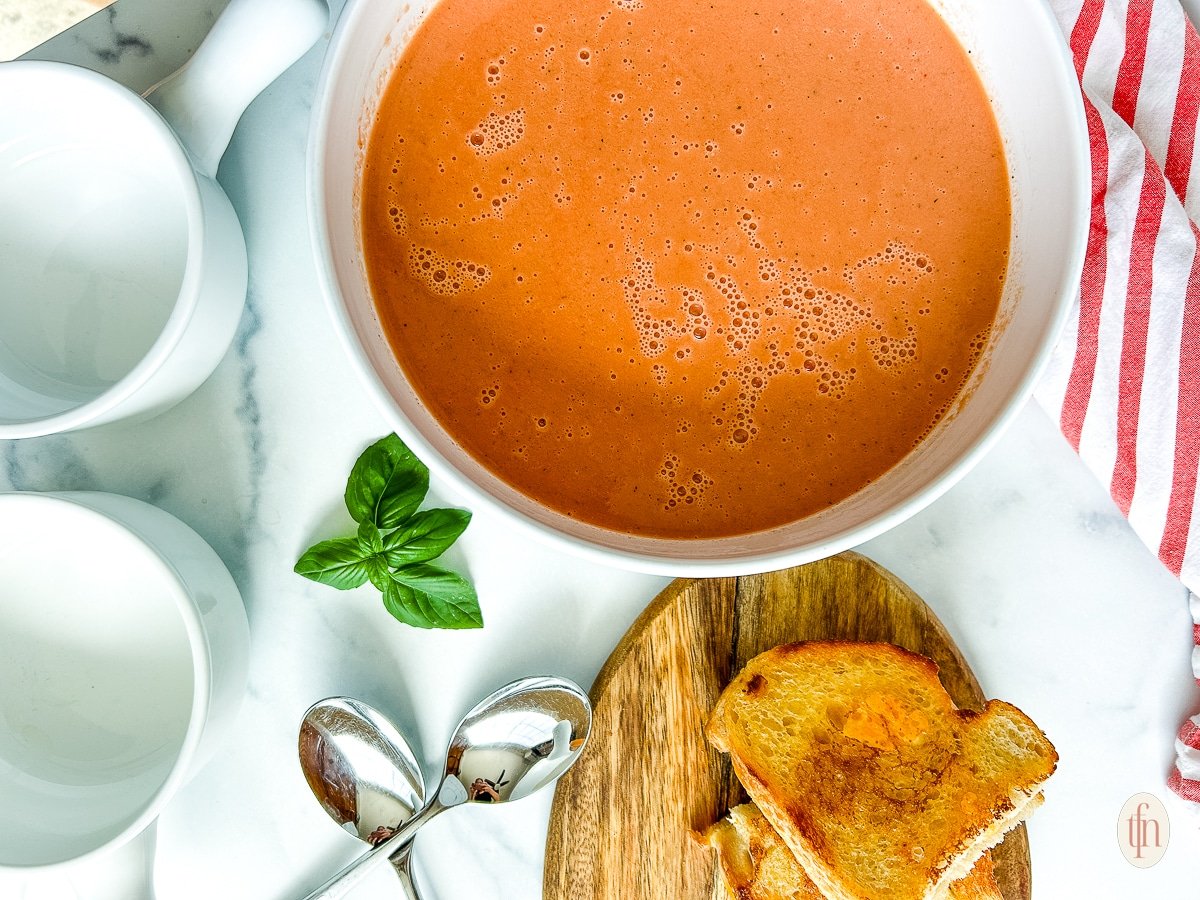 A white bowl filled with 3 ingredient tomato soup and a sprig of basil on the side.