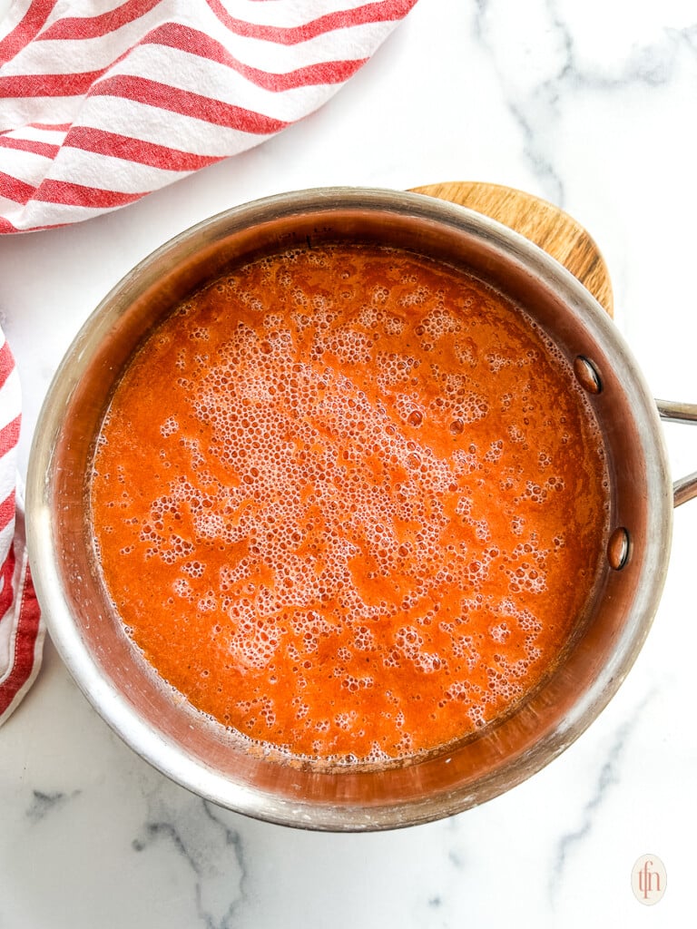 Pot with tomato soup on a white surface.
